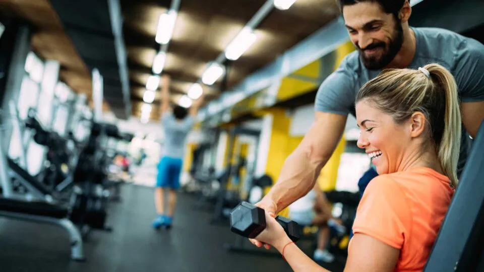Young beautiful woman doing exercises with personal trainer in gym